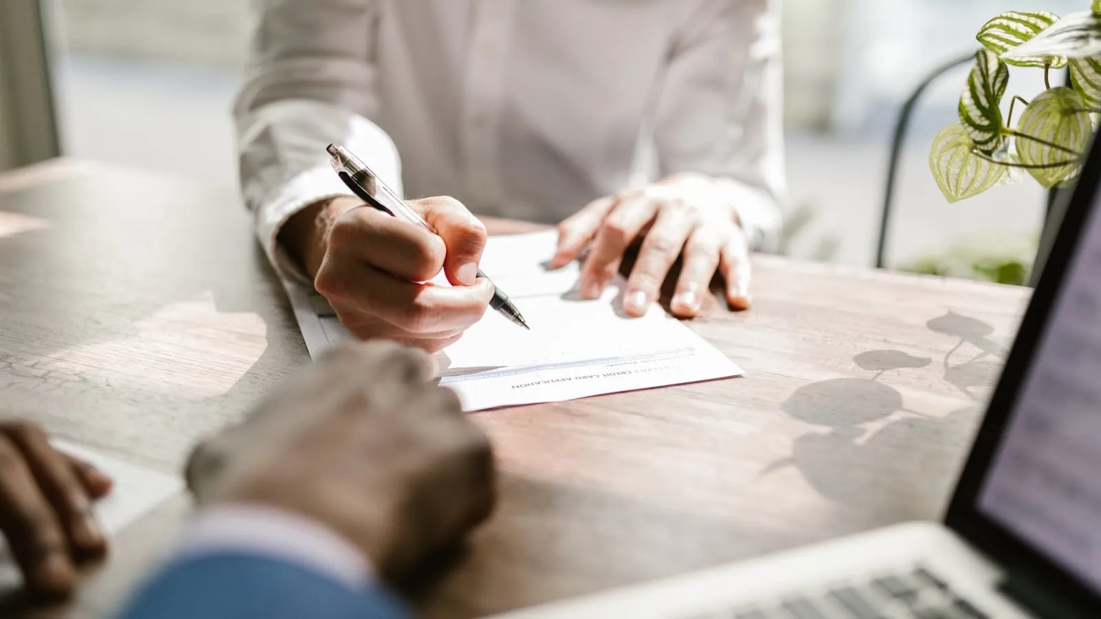 Close-up of a hand signing a document with a pen on a wooden desk, representing the DCT license application and signatory paperwork stage