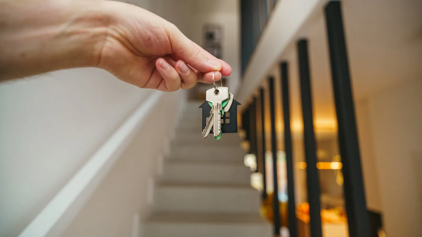 Hand holding house keys with a house-shaped keychain in a modern interior, representing the moment a Dubai property owner begins setting up for short-term rental